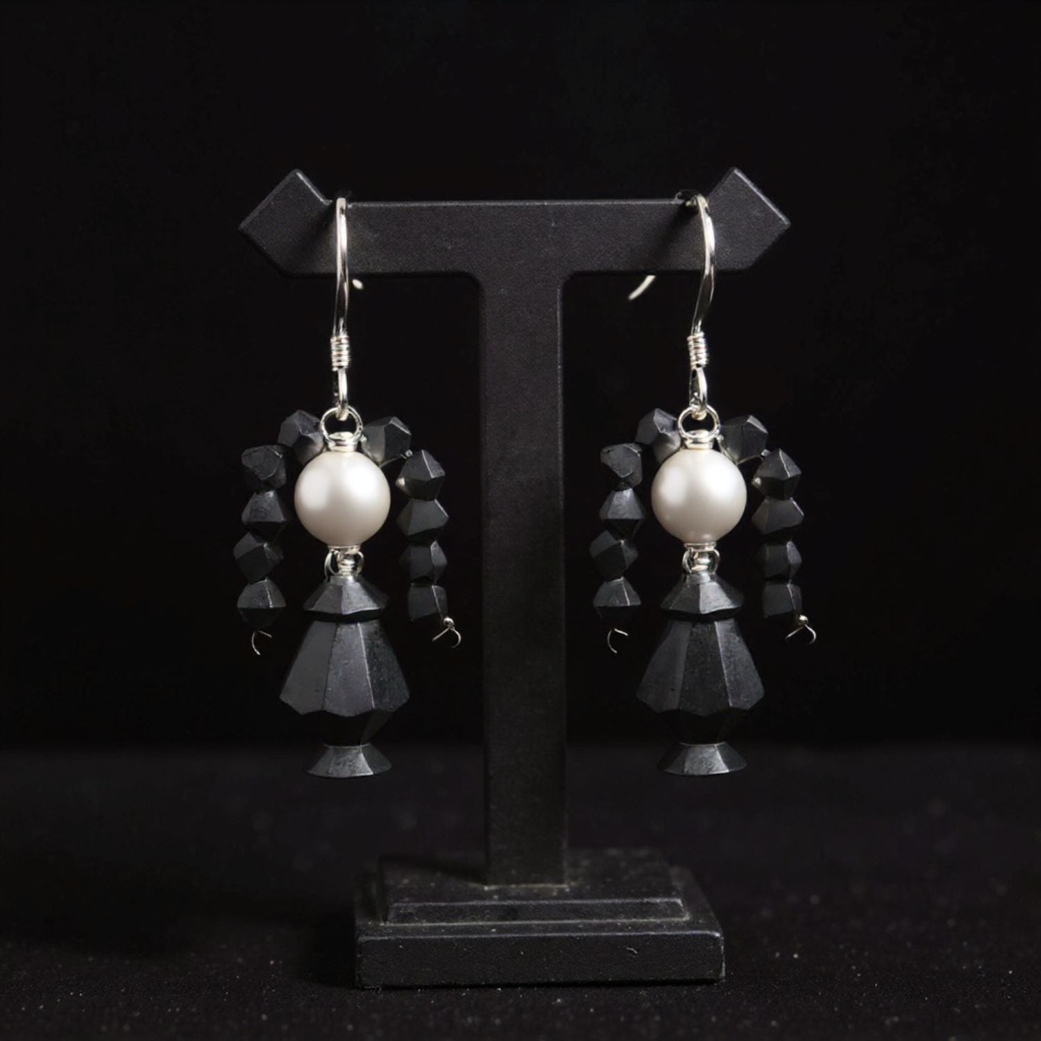 Pair of earrings with black faceted drops and white beads on a black stand.