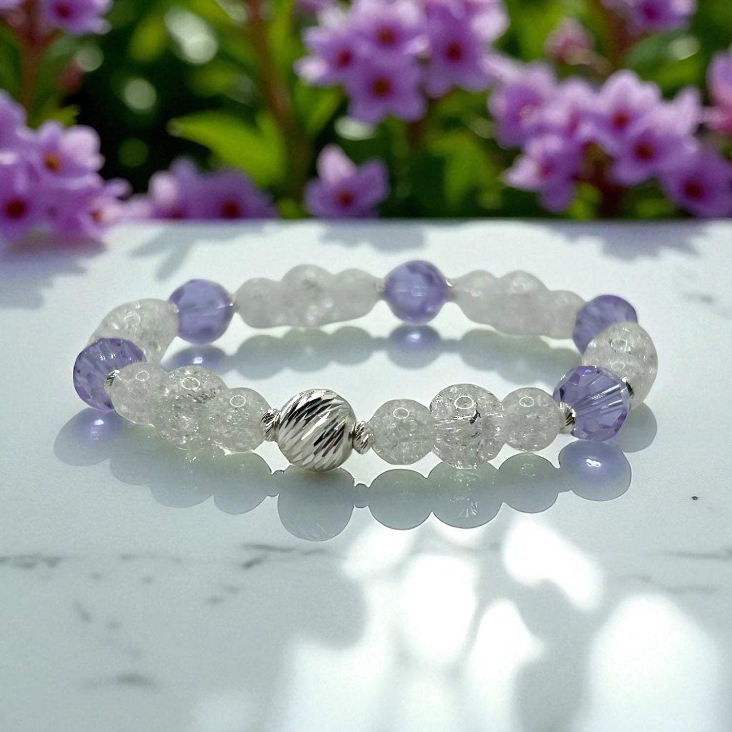 Beaded bracelet with purple and clear beads on a marble surface with flowers in the background