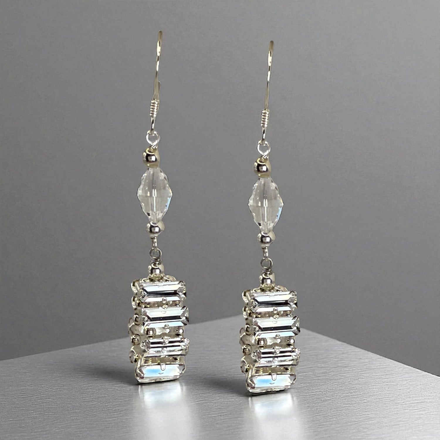 Pair of silver earrings with clear gemstones on a gray background