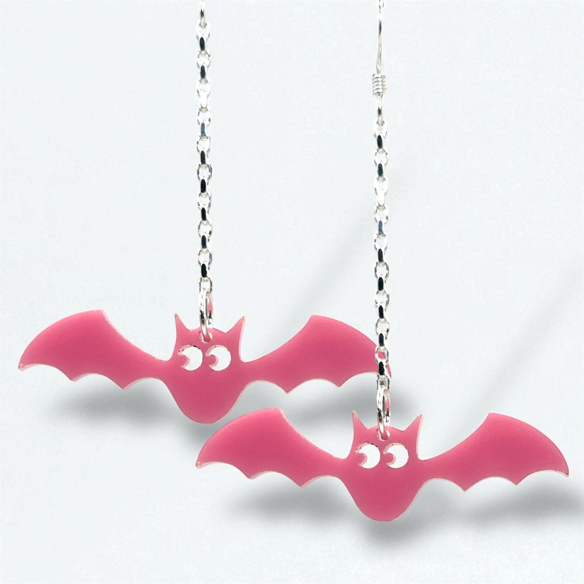 Pink bat-shaped earrings on silver chains against a white background