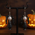 Black and pearl Wednesday Adams earrings on a stand with pumpkins in the background