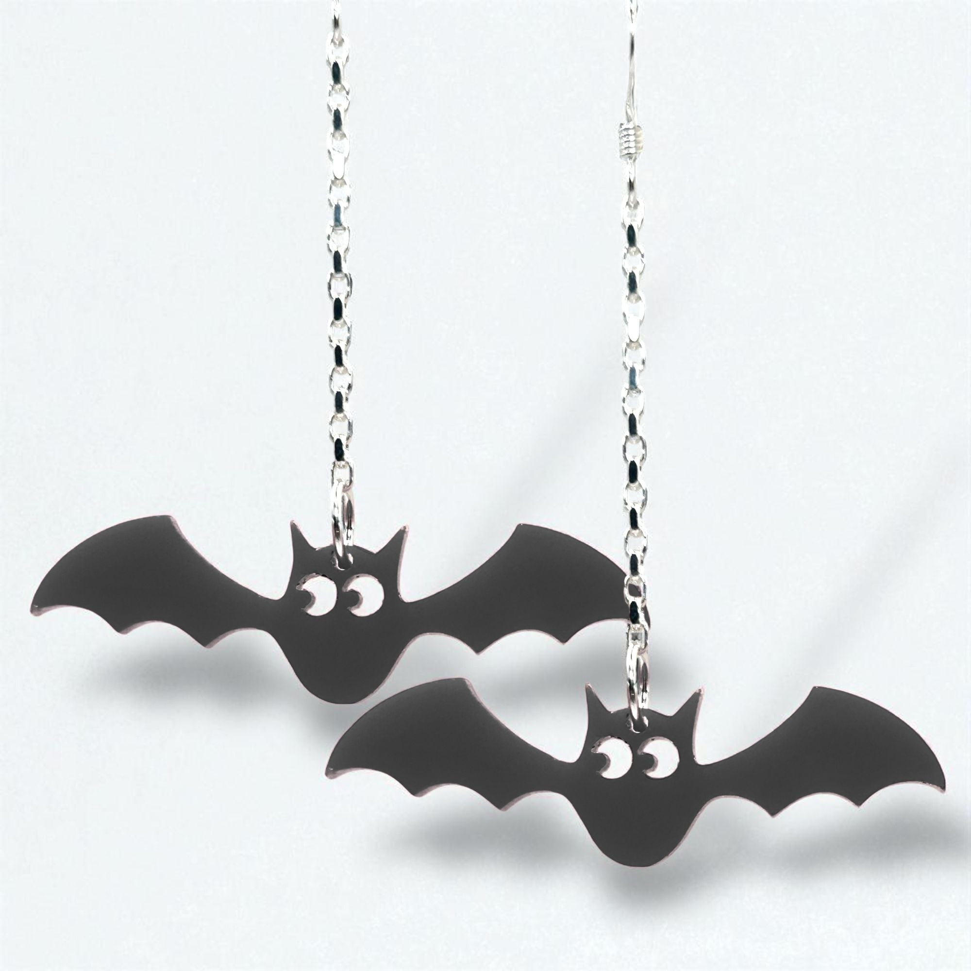 Black bat-shaped earrings on silver chains against a white background