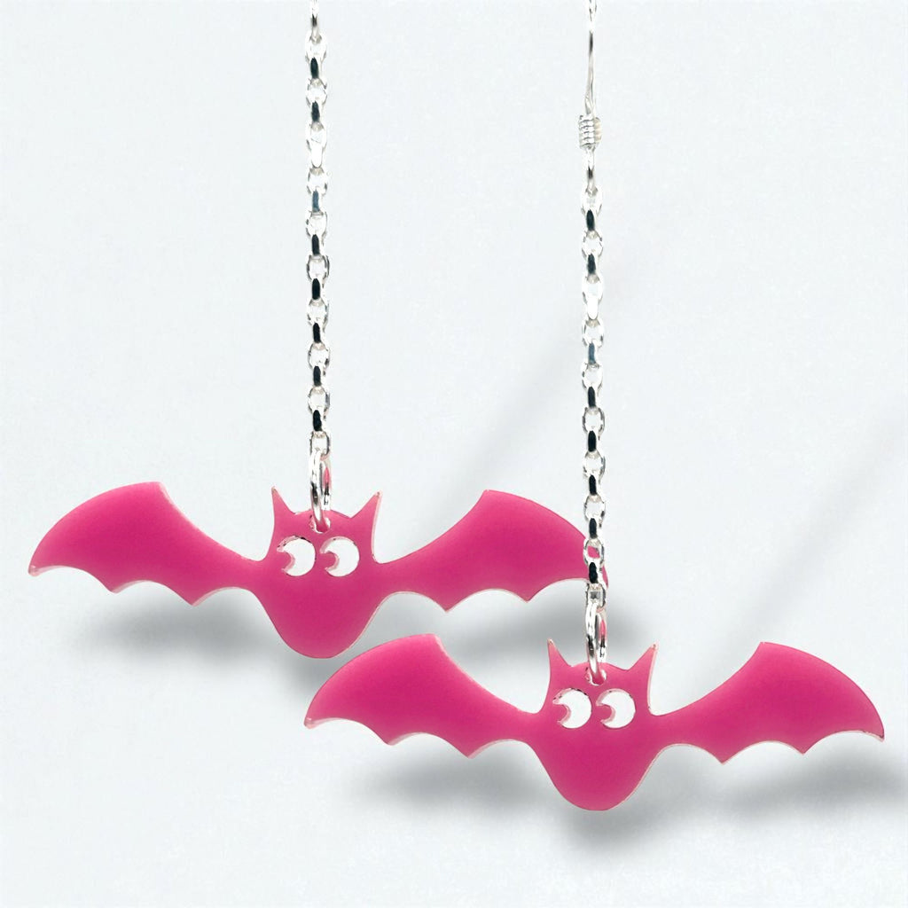 Pink bat-shaped earrings on silver chains against a white background