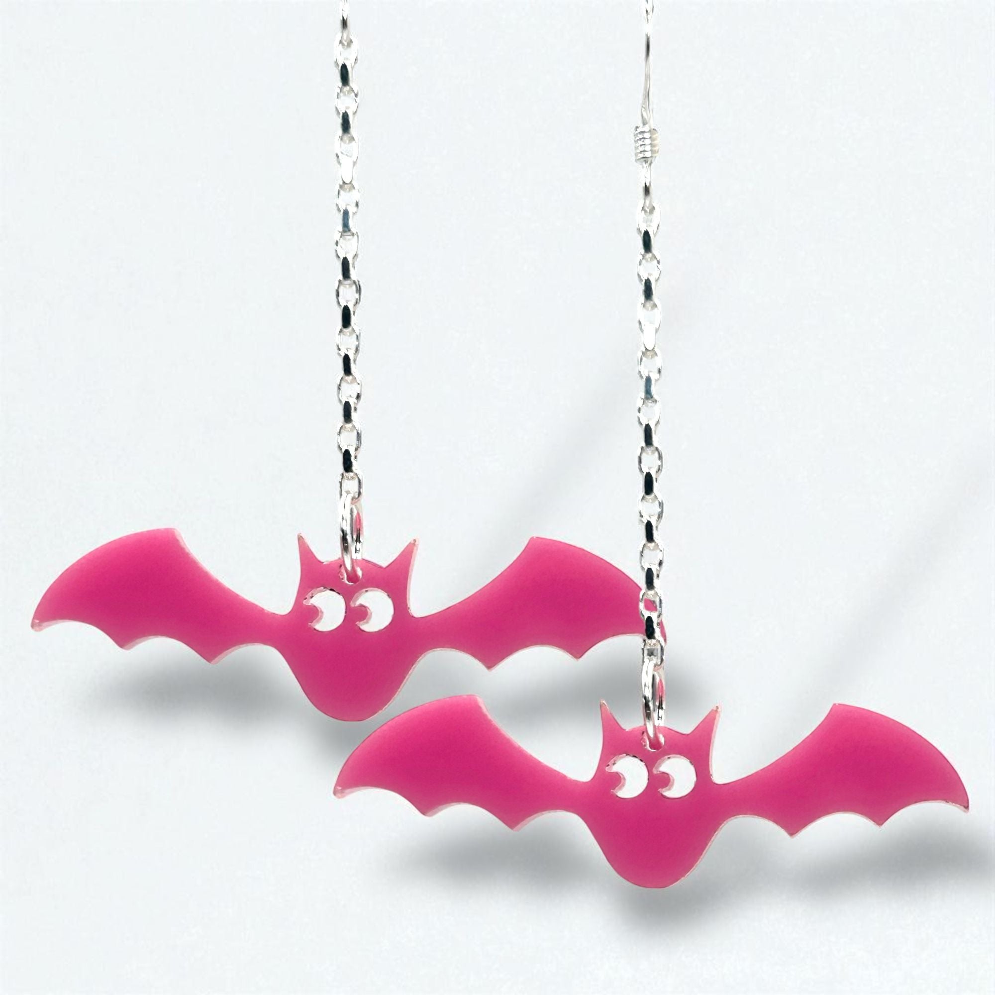 Pink bat-shaped earrings on silver chains against a white background