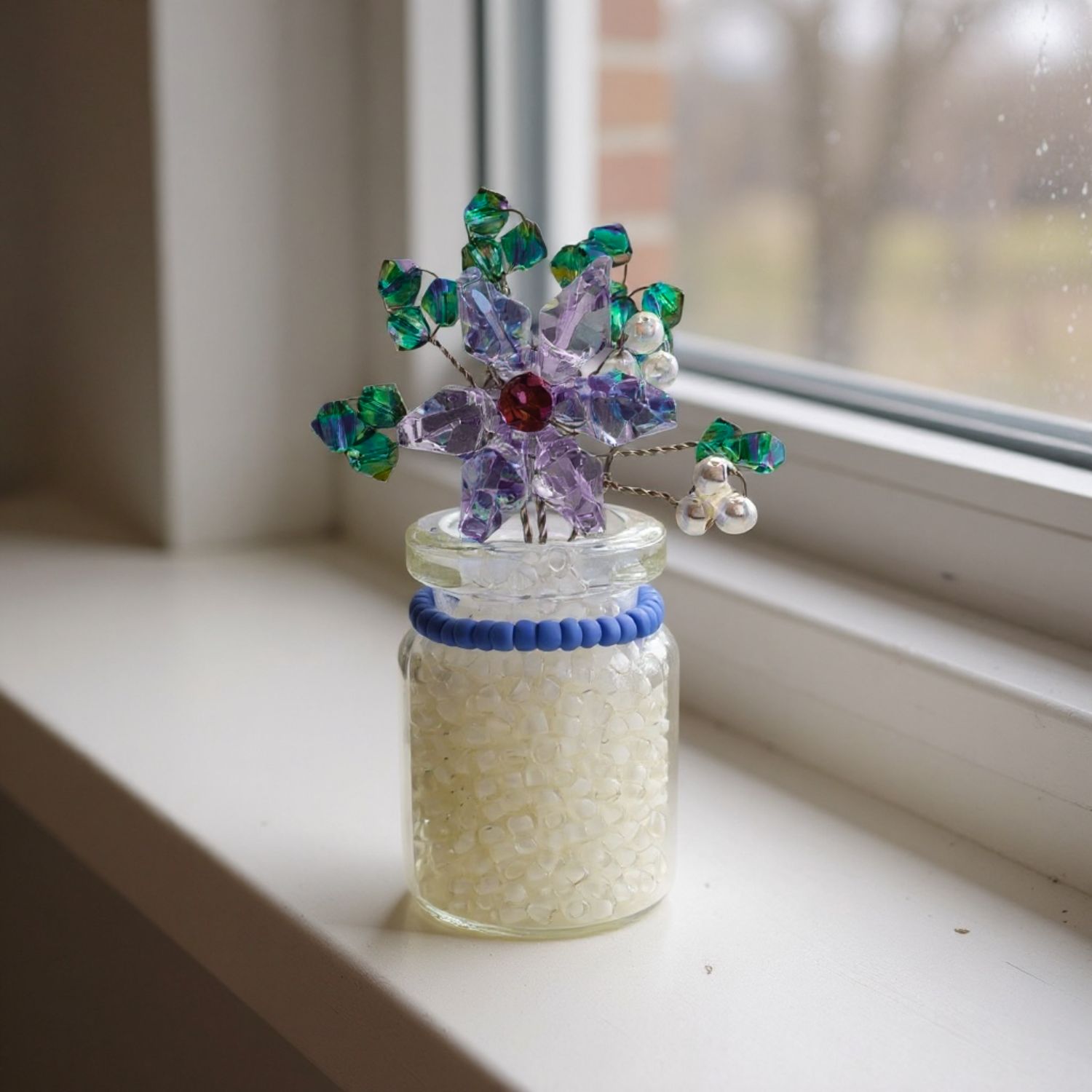 Decorative glass jar with a colorful beaded crystal flower on a windowsill