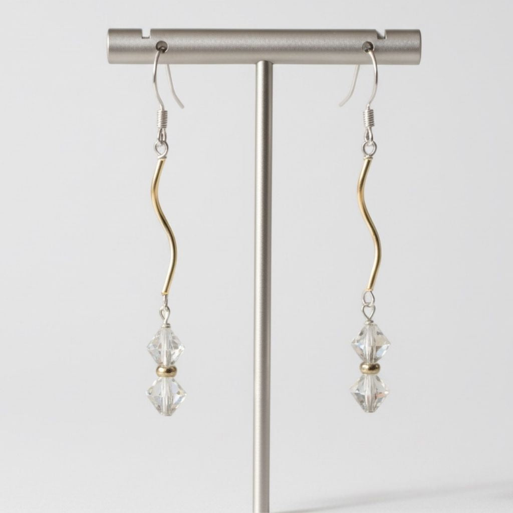 Pair of earrings with clear crystals hanging from a stand against a white background