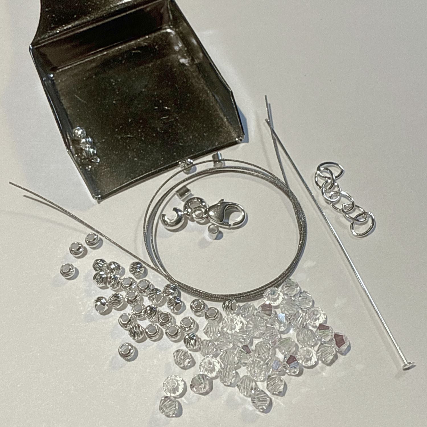 Silver jewelry components including a clasp, chain, and loose beads on a white background