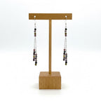 Pair of beaded earrings on a wooden display stand against a white background