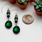 Green beaded earrings with a dime for scale on a white surface with potted plants in the background.