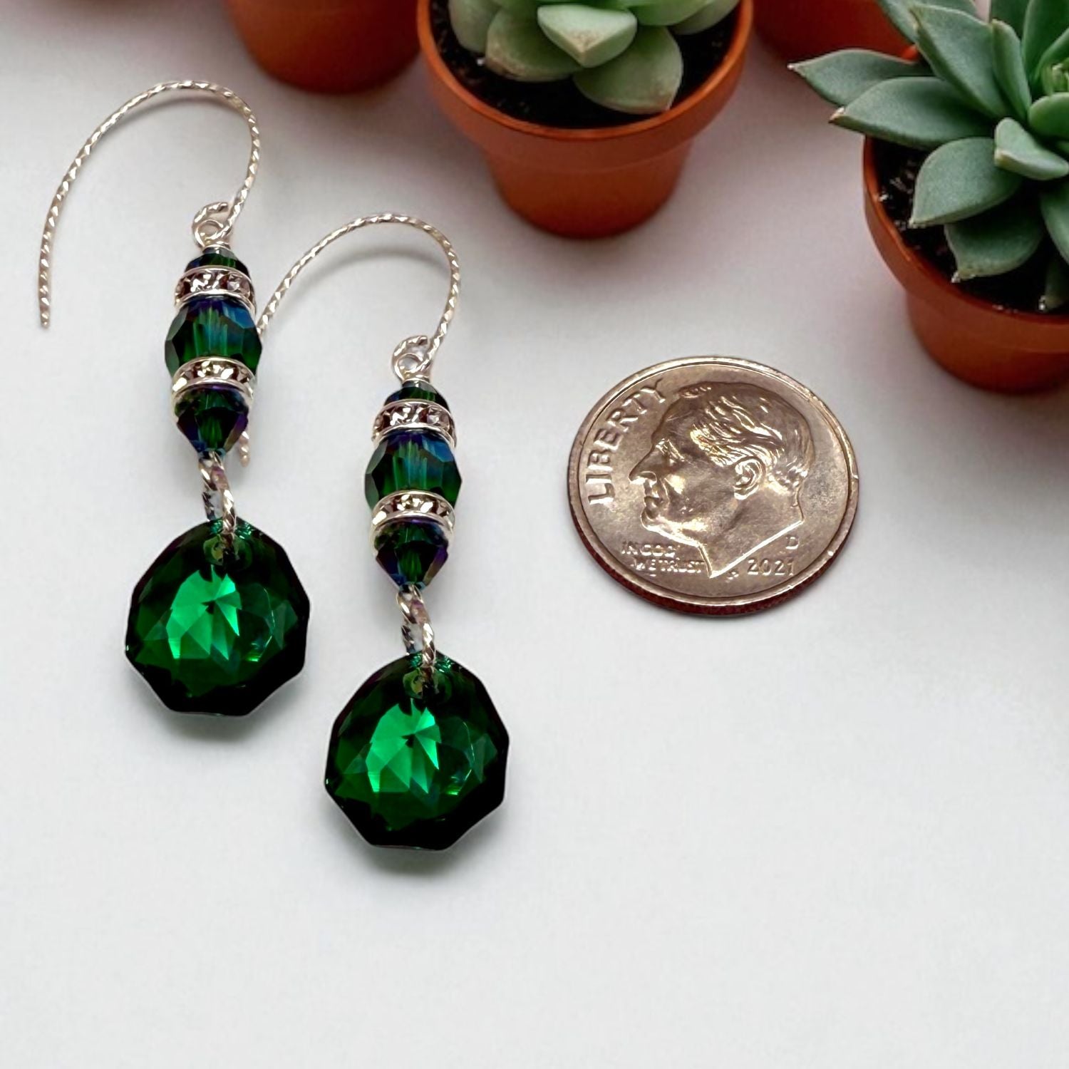 Green beaded earrings with a dime for scale on a white surface with potted plants in the background.