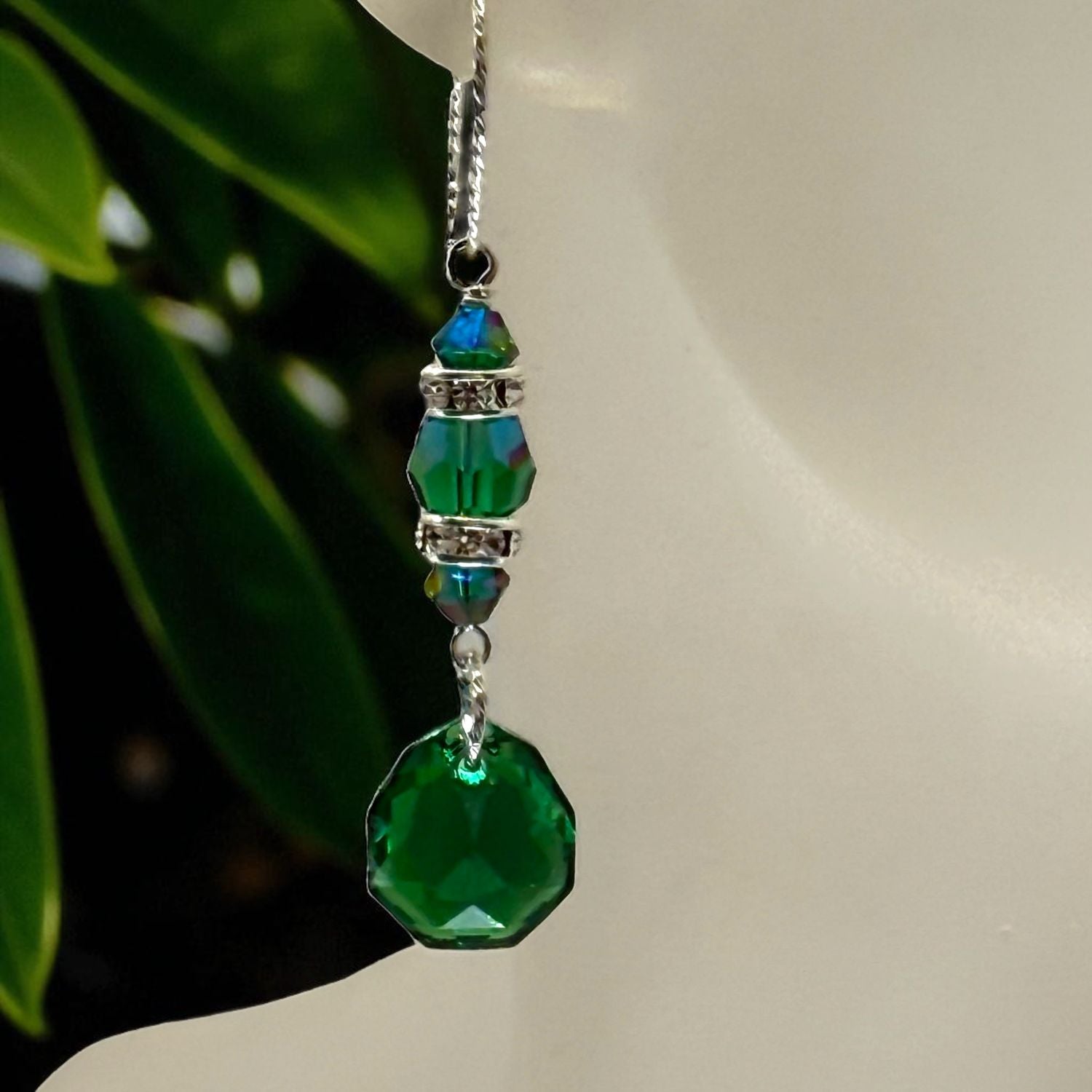Green beaded earring on a mannequin with a blurred green leafy background