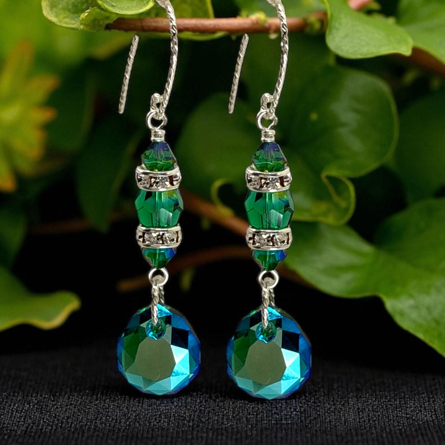Green and blue beaded earrings with silver accents on a black background with green leaves.