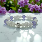 Beaded bracelet with purple and clear beads on a marble surface with flowers in the background