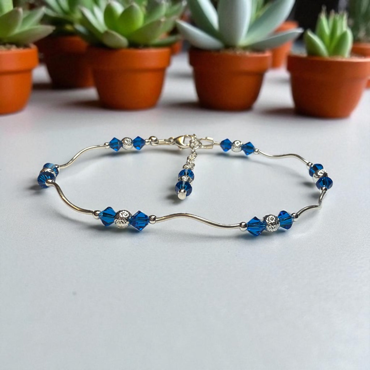 Silver bracelet with blue beads on a light gray surface with potted plants in the background