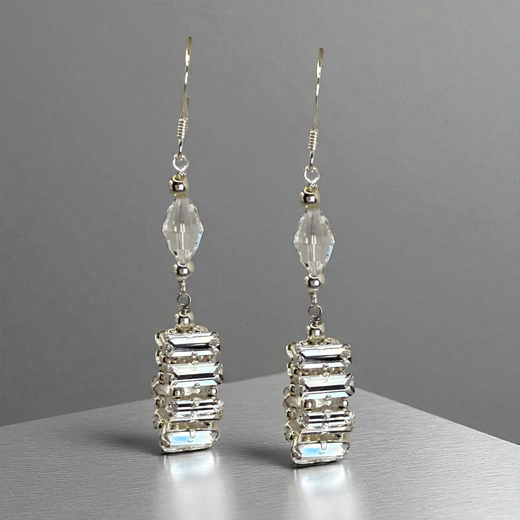 Pair of silver earrings with clear gemstones on a gray background