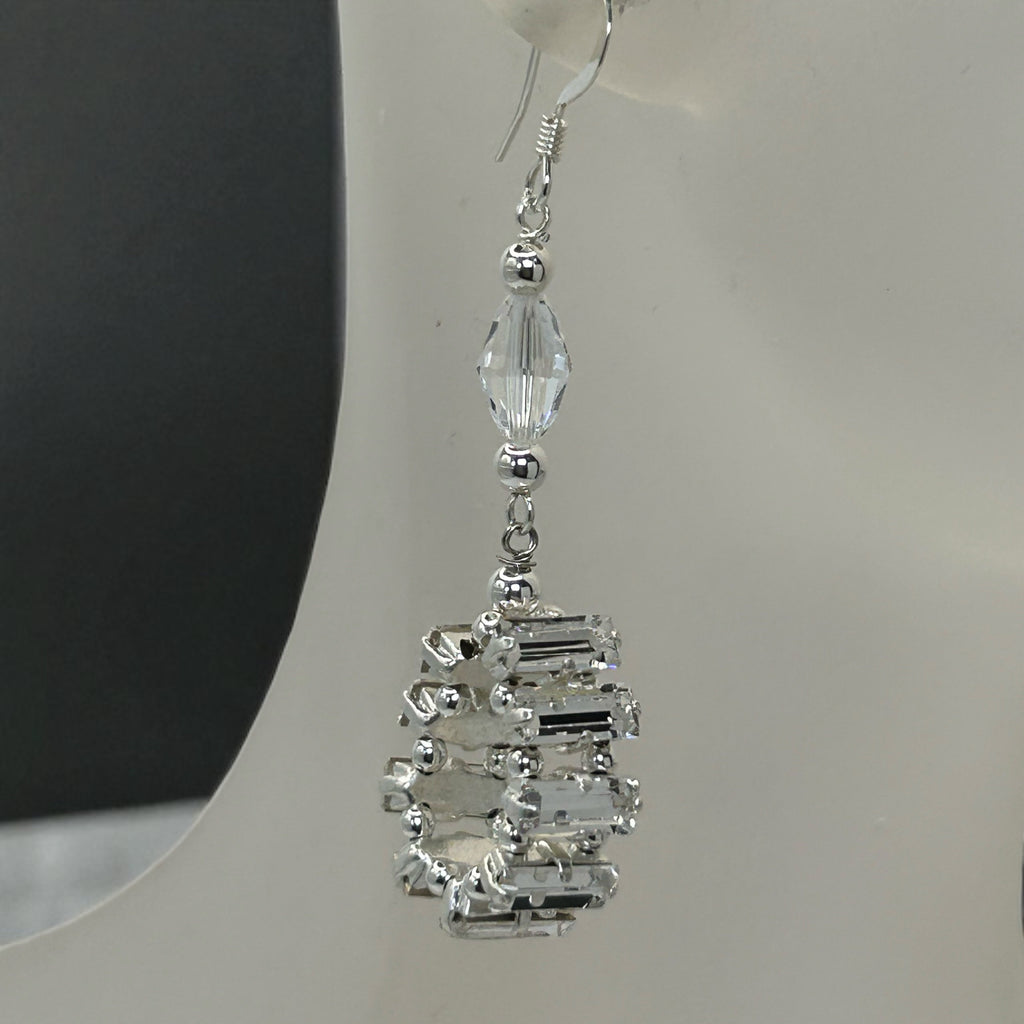 Silver earrings with clear gemstones on a white stand.