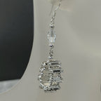 Silver earrings with clear gemstones on a white stand.