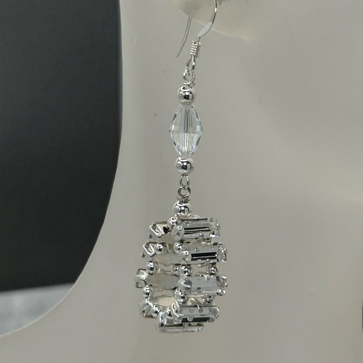 Silver earrings with clear gemstones on a white stand.
