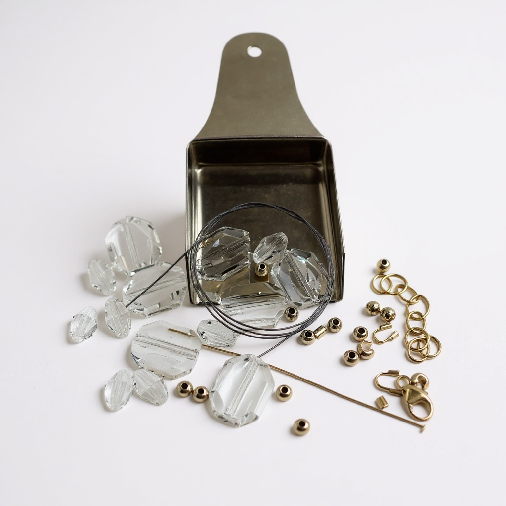 Jewelry-making supplies including clear beads, gold chain links, and a metal scoop on a white background.