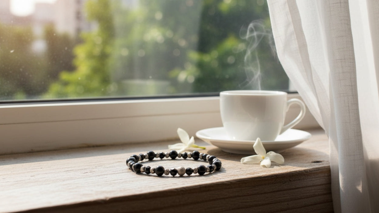 Steaming cup of coffee on a windowsill with a bracelet and white flowers