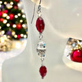 A pair of red beaded earrings with silver crystal embellishments displayed on a mannequin head with Christmas decorations in the background.