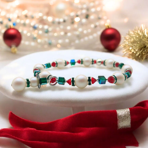 A festive Christmas-themed bracelet featuring a variety of colorful beads including pearls, red bicones, and emerald green crystals, displayed on a white stand with a red ribbon and Christmas decorations in the background.