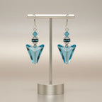 Pair of blue triangle earrings on a metallic stand against a beige background