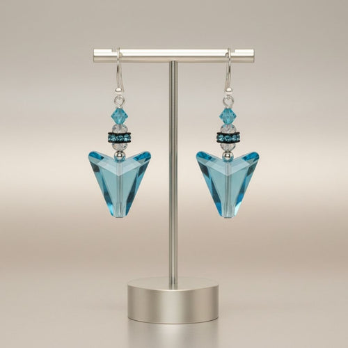 Pair of blue triangle earrings on a metallic stand against a beige background