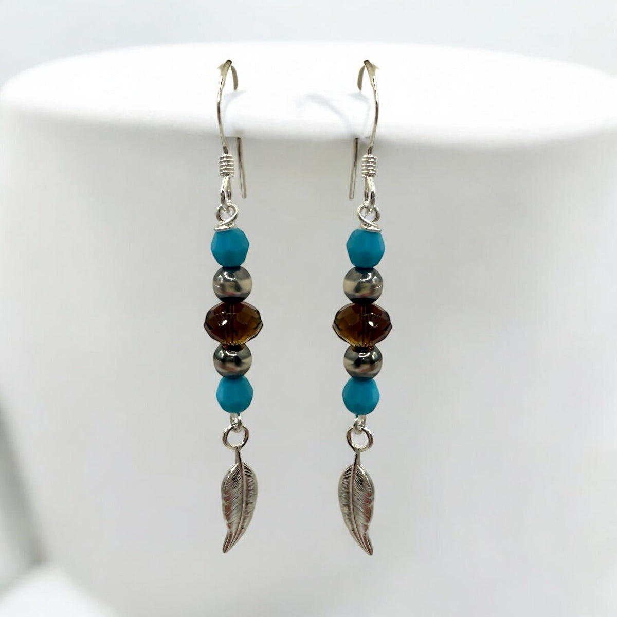 Add a touch of nature to your style with the Ready to Wear Turquoise Feather Earrings from Too Cute Beads! These handcrafted earrings feature Swarovski Mocca Briolette Beads for a warm, rich glow, paired with Sterling Silver Navajo Beads, Turquoise Swarovski Rounds, and delicate Sterling Silver Feather Charms that dangle gracefully. With a length of approximately 2 inches, these lightweight earrings offer a bohemian flair perfect for everyday wear or special occasions.