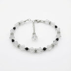 A beaded bracelet featuring faceted clear crystal beads and small black beads, with silver-toned metal links and a dangling crystal charm, shown on a plain white background.