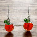 A pair of handmade earrings crafted from orange and green beads, designed to resemble pumpkins, complete with green leaf-like beads on sterling silver ear wires.