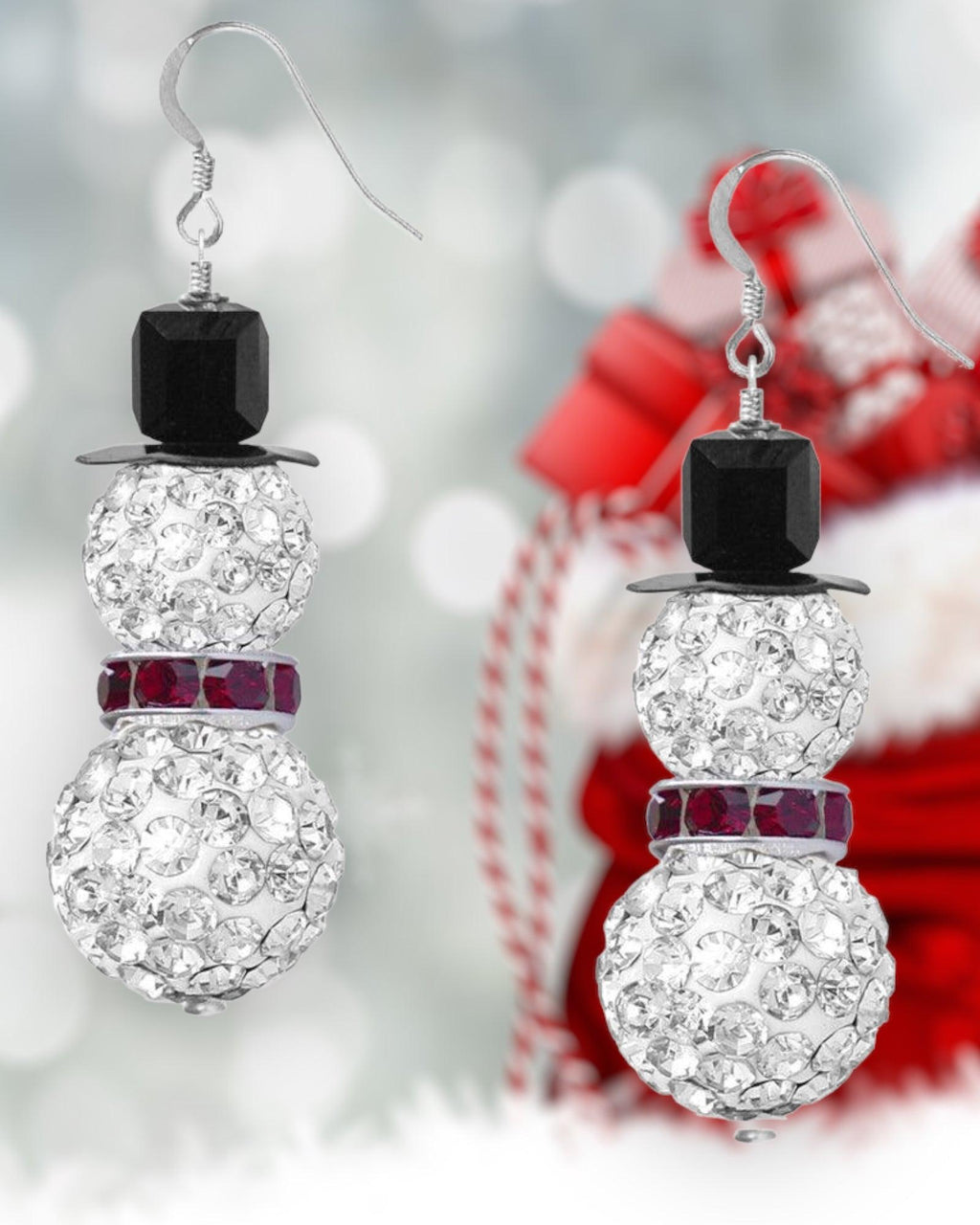 A photo showing a pair of pave snowman earrings with black, silver, and red beads against a festive Christmas themed background.